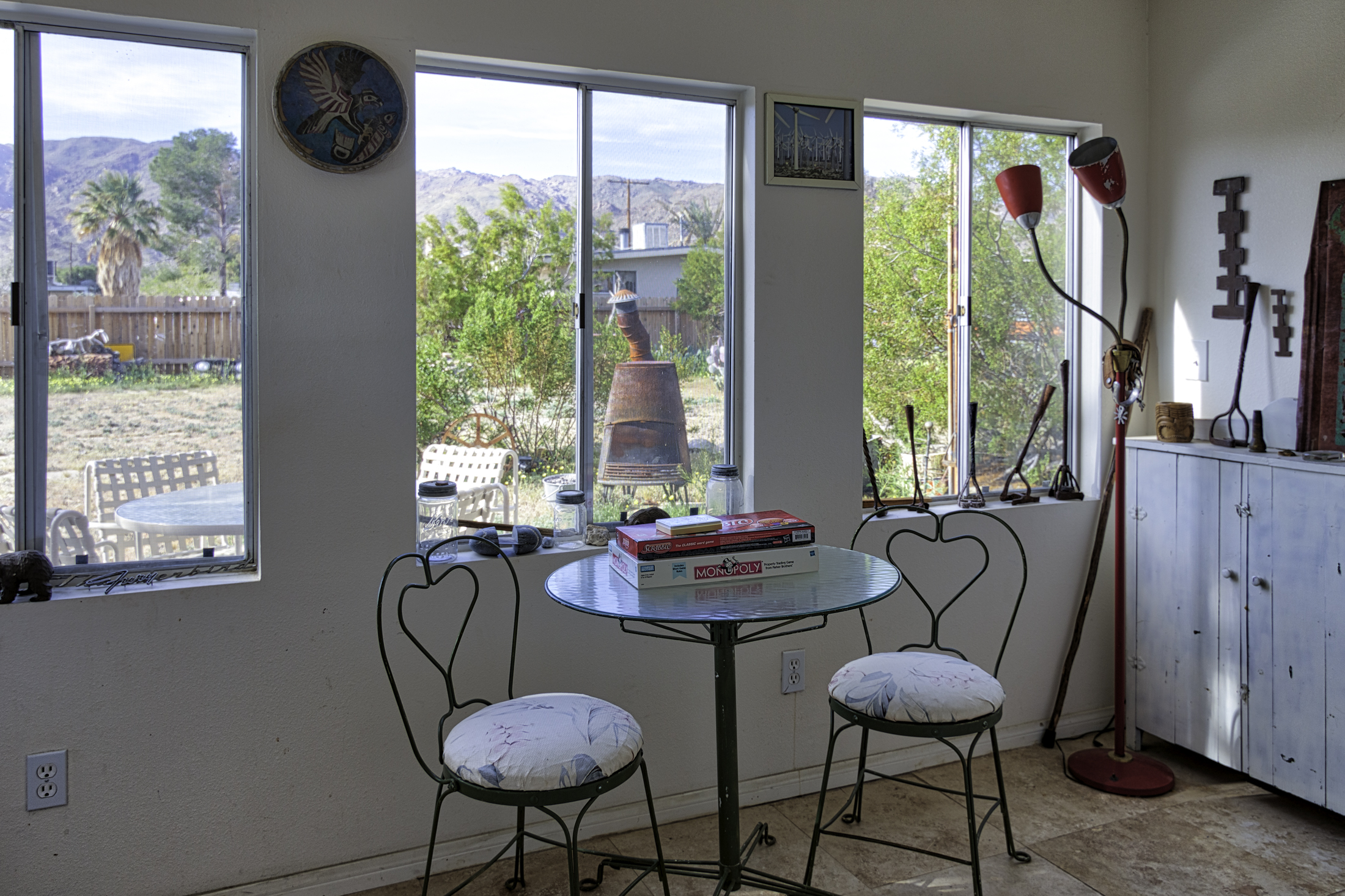 A sun room with view of small round glass table and windows viewing into the yard of the vacation rental and various rustic items on the window sills.