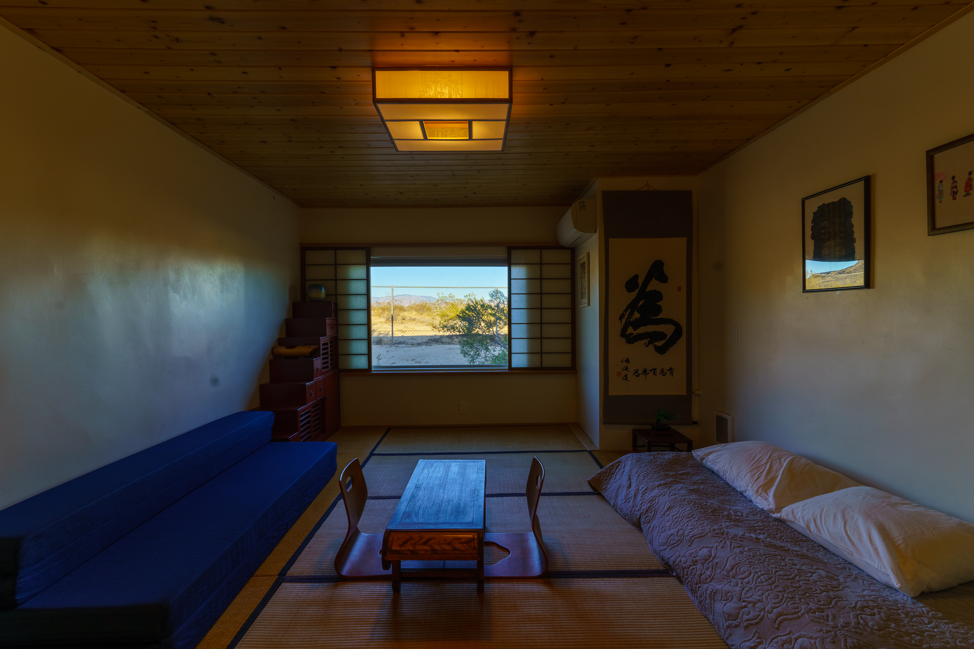 A room with tatami mat flooring, futons, and Japanese style wall decorations with evening lighting.