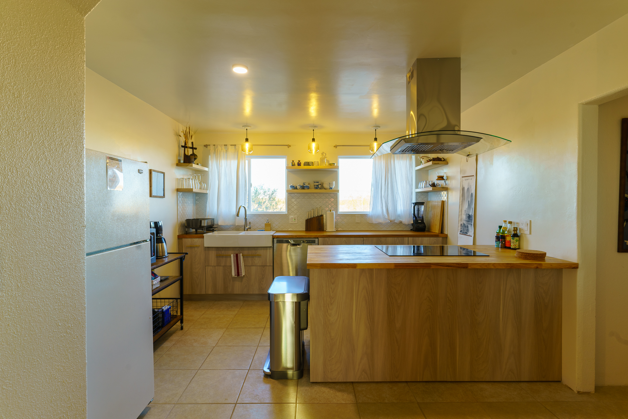 A medium sized kitchen with sink, dishwasher, blender, coffee pot, microwave, trash can, stove oven, and plenty of dish ware.