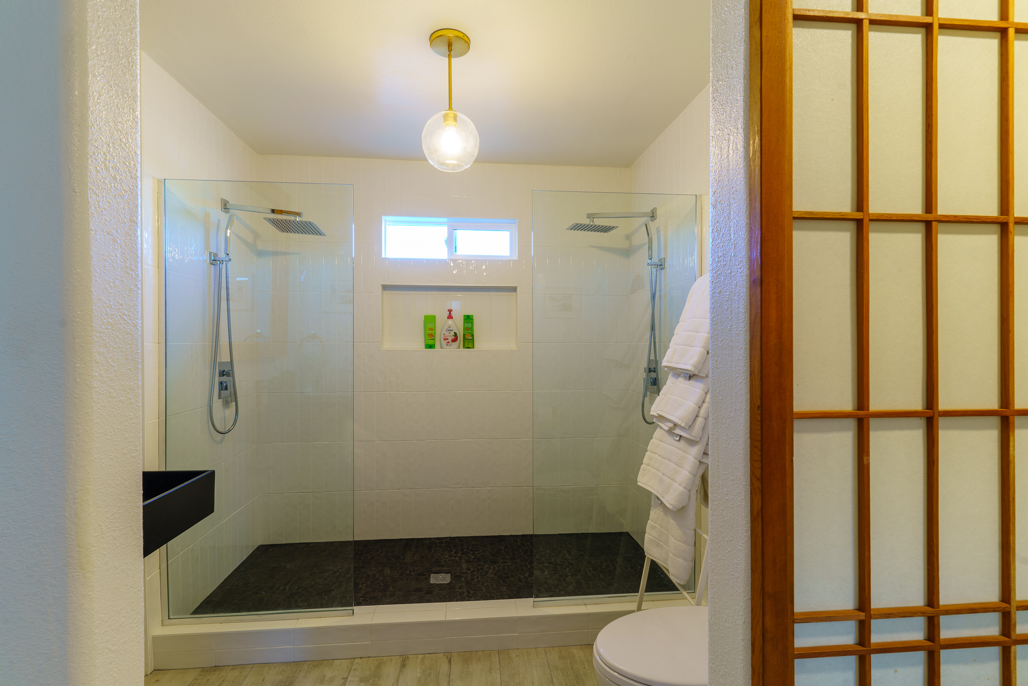 A bathroom with a toilet, sink, and glass shower with two shower heads.