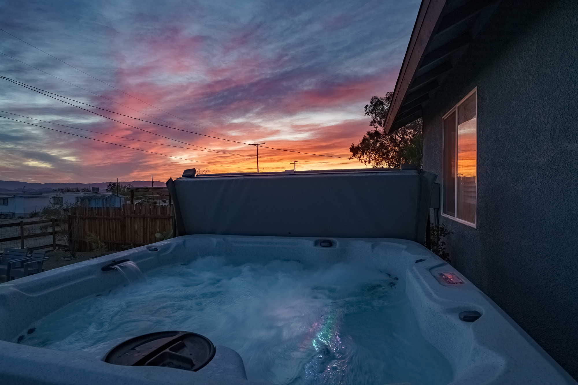 A relaxing hot tub in the foreground with a beautiful desert sunrise in the background, featuring pink and orange clouds and the rising sun.