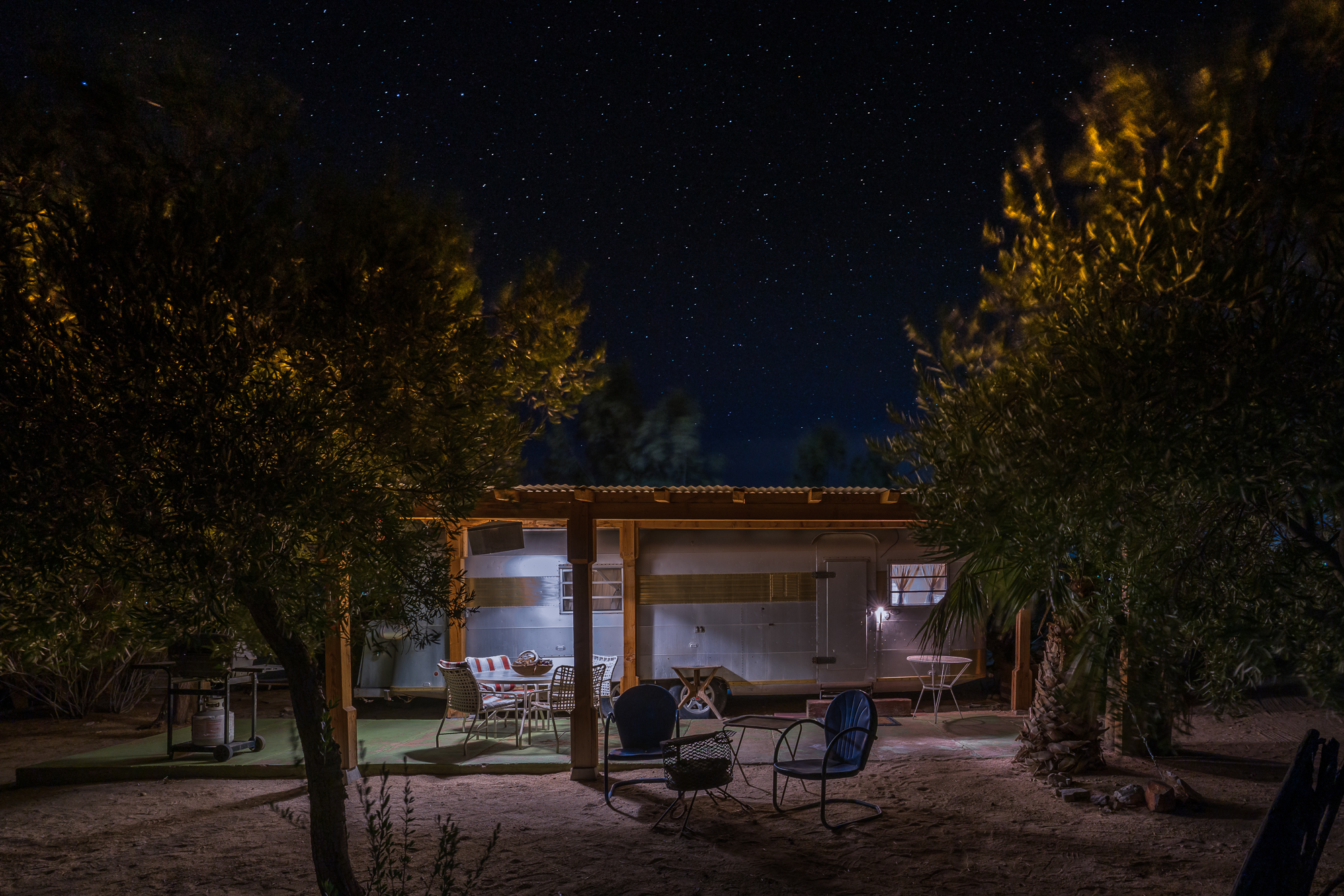vintage silver streak trailer surrounded by olive trees and night with clear starry skies above