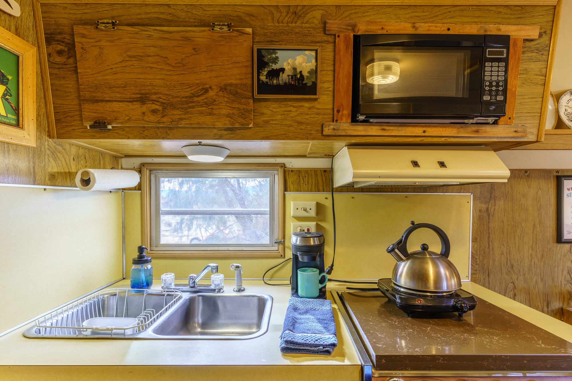 A kitchenette with sink, dish rack, tea kettle, coffee machine, small camping stove, and a microwave.
