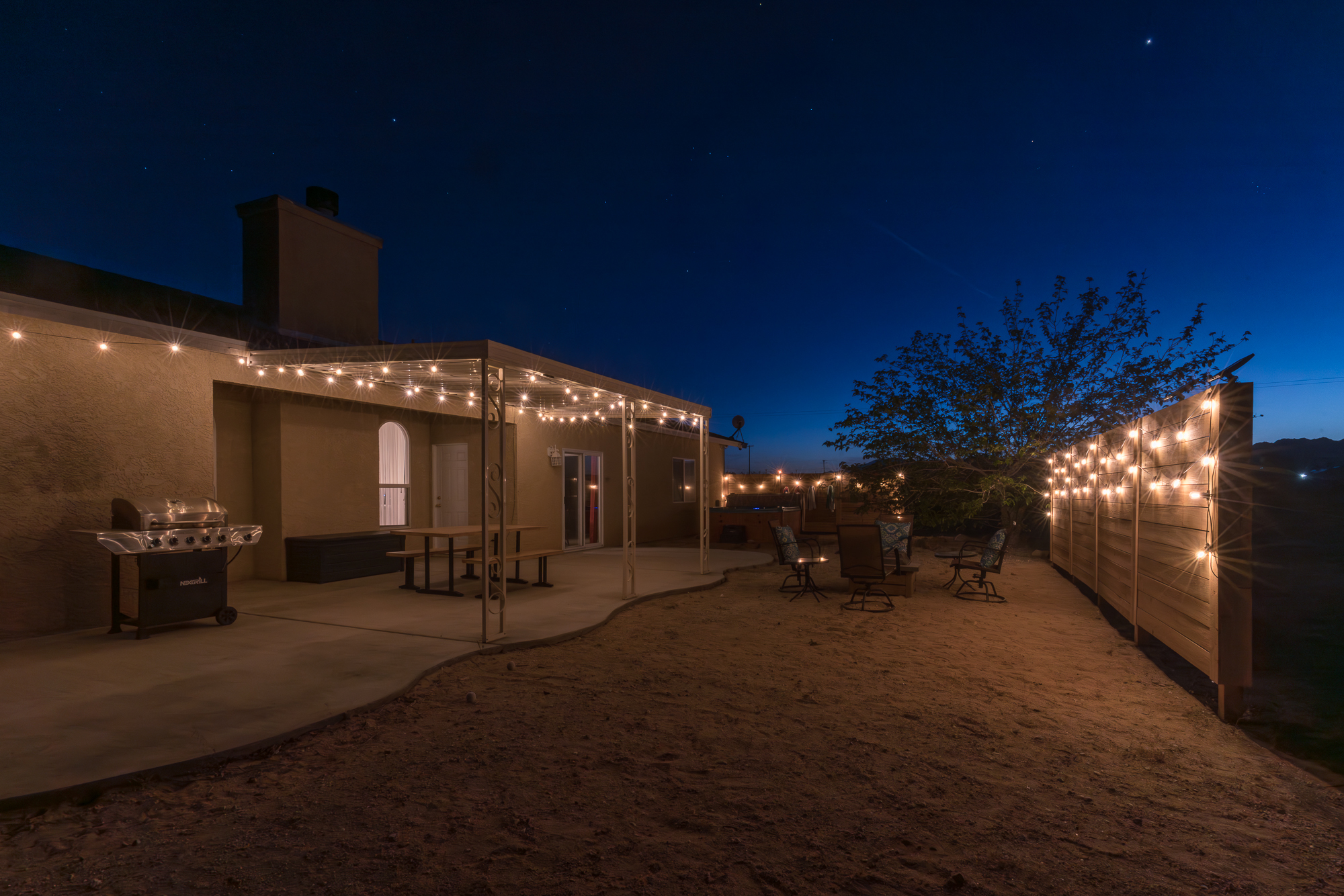view of the backyard at civil twilight with solar lighting, firepit area, covered patio and a hot tub