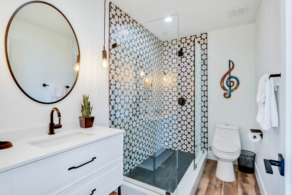 a Bathroom with a Modern Vanity, Circular Mirror, Stylish Tile Shower, and Decorative Elements.