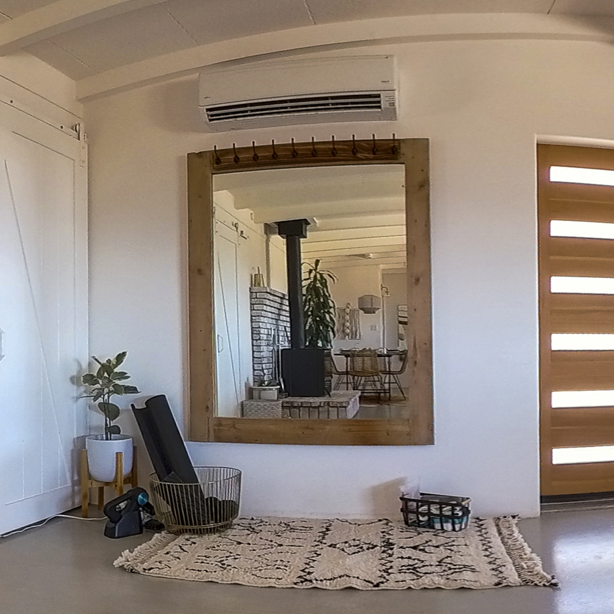 Workout Area Inside Casa Coyote Living Room Featuring a Large Wood-framed Mirror, Yoga Mats, Light Weights, a Patterned Rug, Indoor Plants, and a View of the Dining Area Reflected in the Mirror.